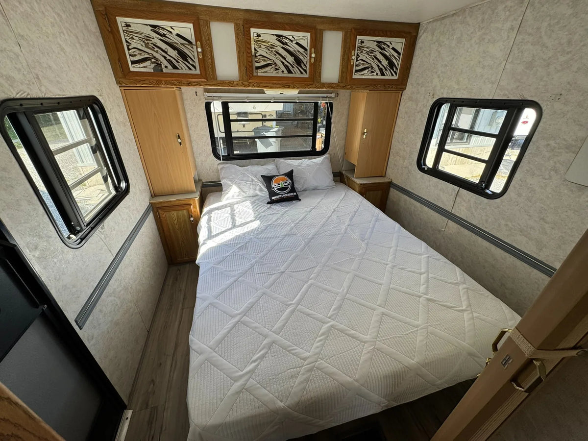 Chambre de la Sportsmen 3000 avec grand lit, trois fenêtres et armoires au-dessus de la tête de lit.