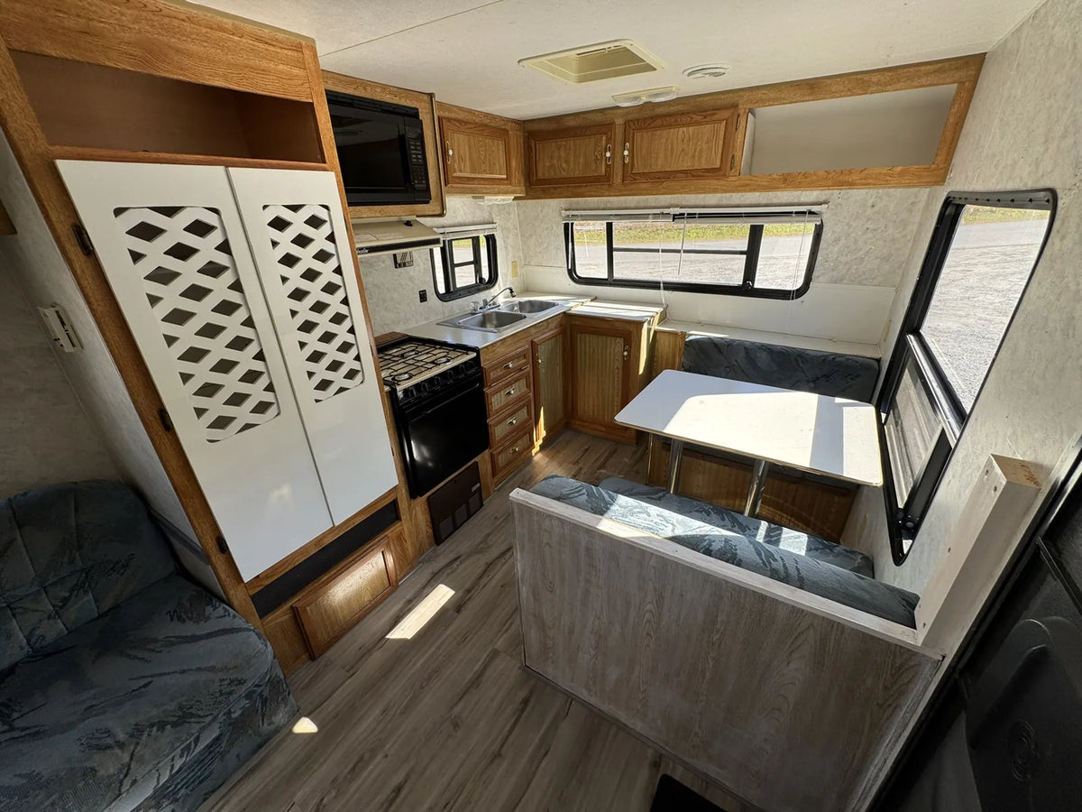 Cuisine de la Sportsmen 3000 avec cuisinière, évier, armoires et dinette près des fenêtres.