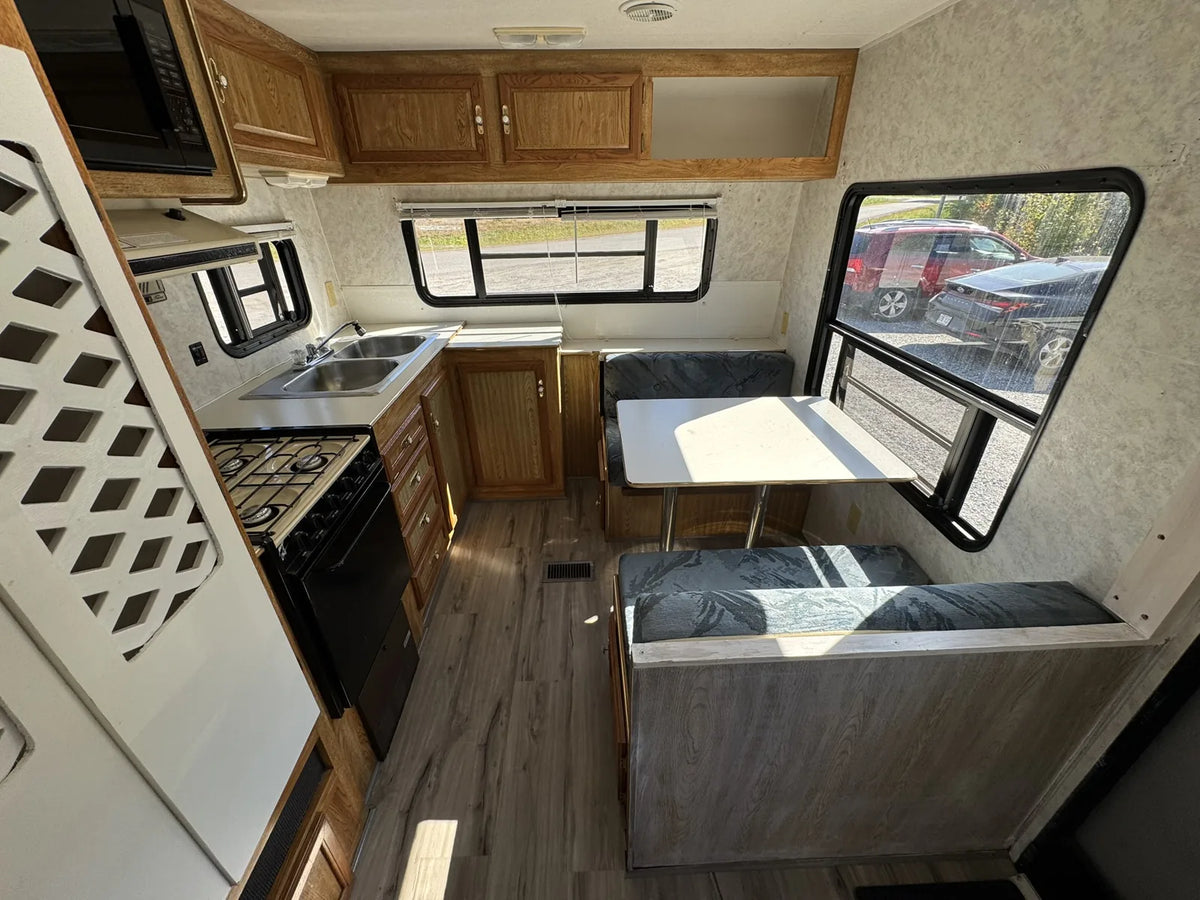 Dinette de la Sportsmen 3000 avec table, banquettes, grandes fenêtres et cuisine avec évier et cuisinière.