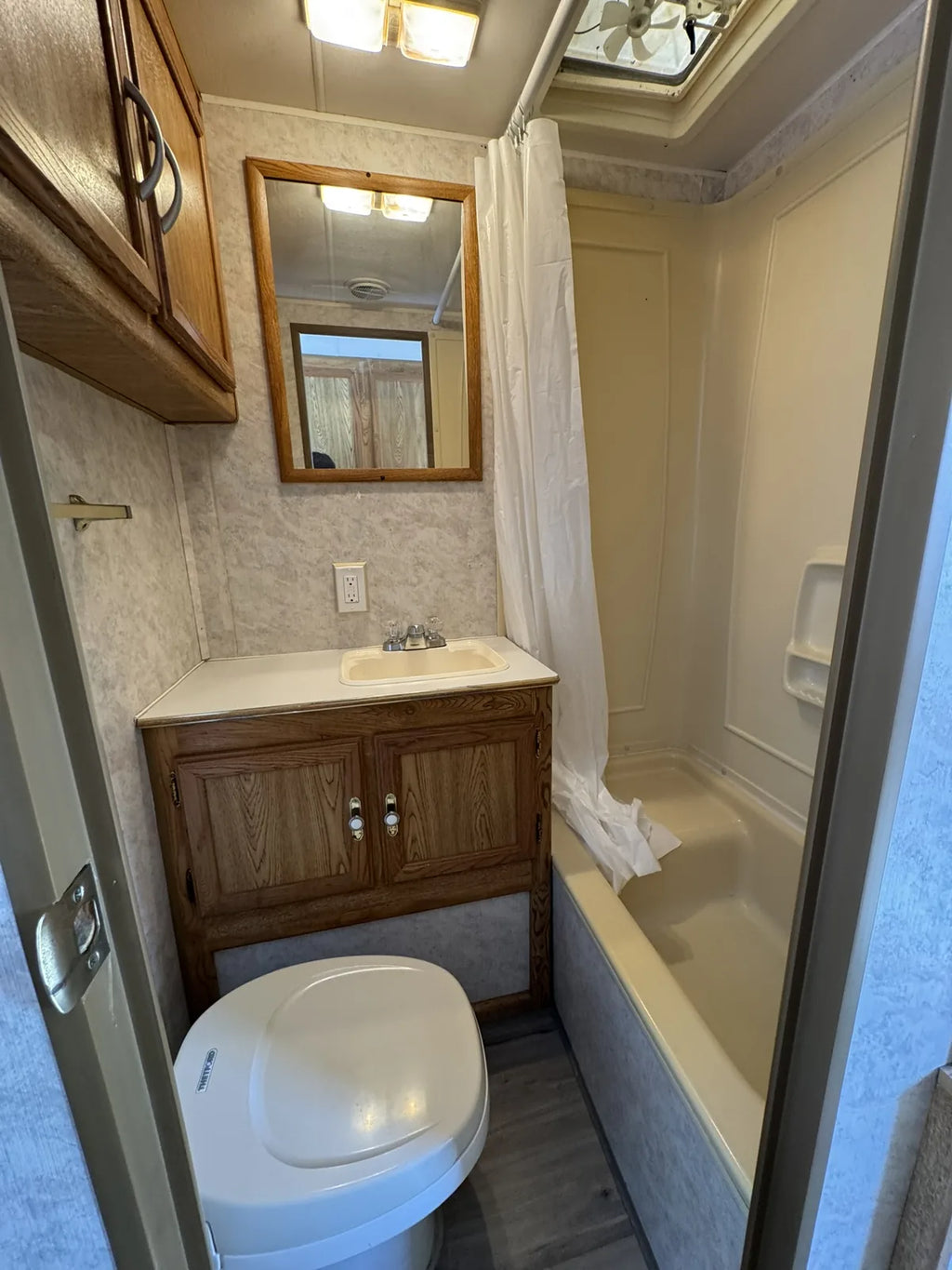 Salle de bain de la Sportsmen 3000 avec toilette, lavabo, miroir et bain-douche à rideau.