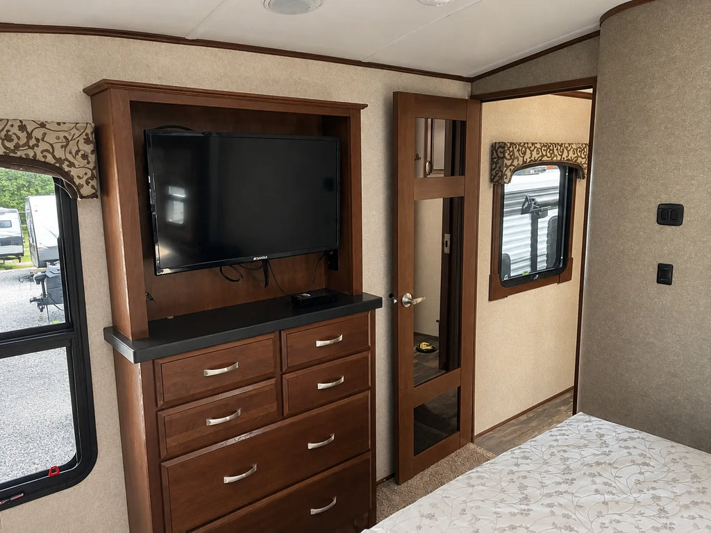 Téléviseur au-dessus d’une commode en bois dans la chambre de la Jayco Pinnacle 36KPTS 2017, près de la porte avec miroir.