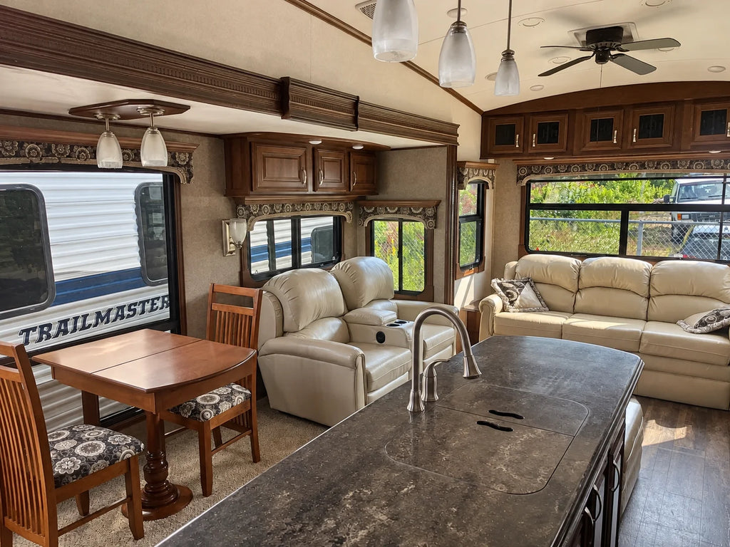 Salon de la Jayco Pinnacle 36KPTS 2017 avec divan, deux fauteuils, table à manger et grandes fenêtres, vu depuis l’îlot de cuisine.