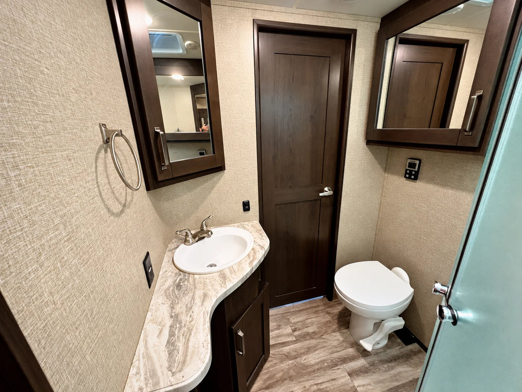 Salle de bain de la Reflection 28BH 2021 avec lavabo, comptoir, armoires à miroir, toilette et douche vitrée.